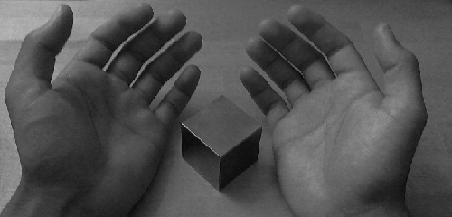 Hands around metal cube.